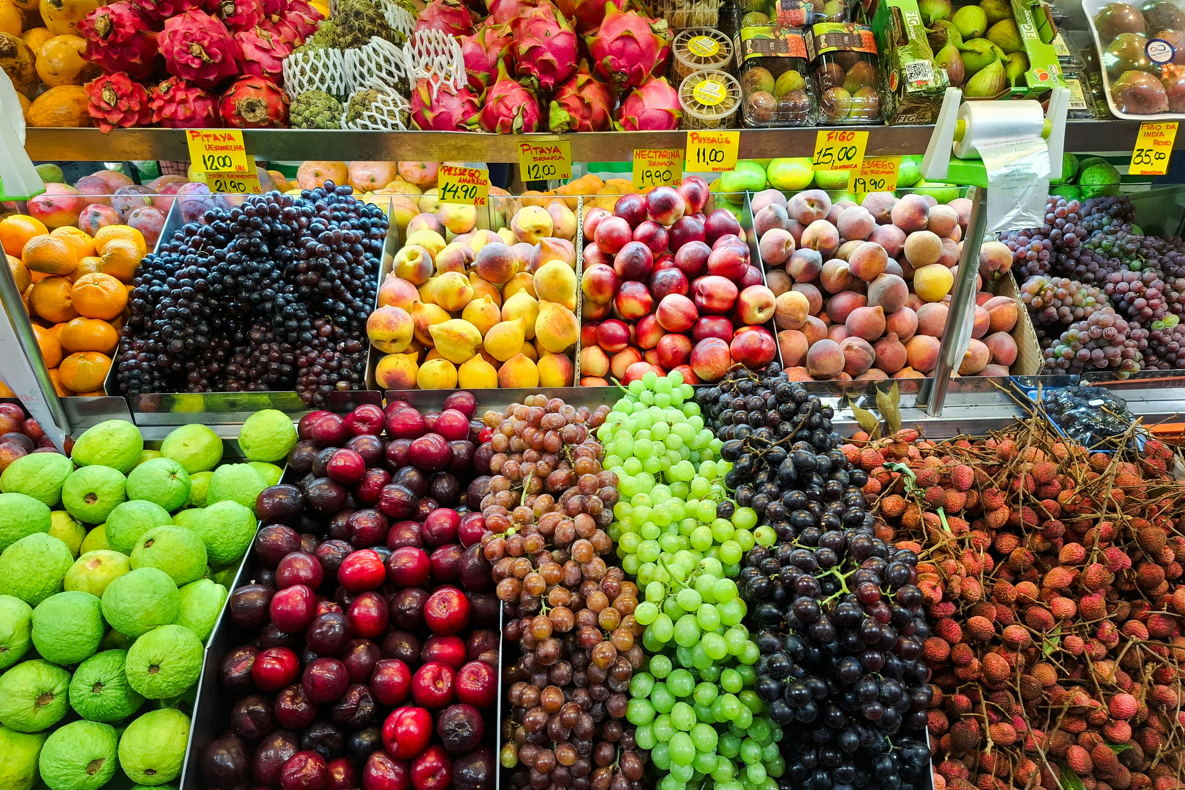 Colorful assortment of fresh fruits including apples, oranges, grapes, and lychees at a market.